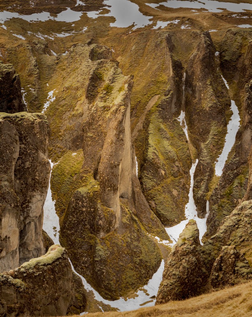 A Lord of the Rings looking formation in an Iceland canyon - mossy, dramatic spire, with snow drifts