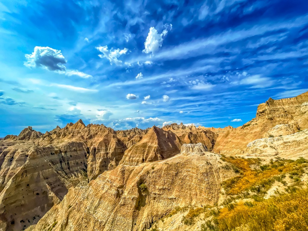 A hot summer day at the Badlands in South Dakota. Storms create interesting white and blue skies agains the yellows, and oranges of the rock formations. 