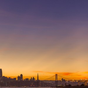 Golden rays of sunset beam from behind the silhouetted city of San Francisco